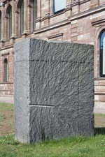 Ein Granitblock in drei Teile gespalten; der mittlere Teil in vier Teile geschnitten. Alle Teile zur ursprünglichen Blockform zusammengefügt, der untere Teil als Fundament in die Erde eingelassen.