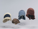 Beiger Damenhut, helmförmige Kappe, links aufgeschlagene Krempe, darüber tropfenförmiger dunkelblauer Filzeinsatz im Kopf, der sich zu einem umlaufenden Streifen verjüngt
